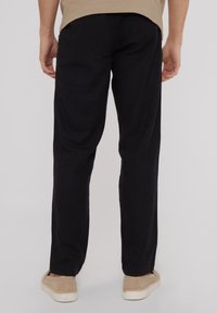 Pantalones de lino negros con un diseño de pierna recta, que presentan una textura suave y un sutil pespunte. Combinados con unos zapatos de lona beige.