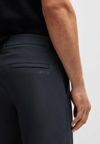 Dunkelblaue Hose aus glattem Stoff, mit einer Gesäßtasche und geprägtem Logo-Detail. Schmaler Schnitt mit einem mittelhohen Bund.