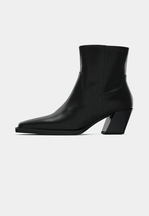 Zwarte leren enkelboot met een spitse neus, een slanke silhoeet en een chunky vierkante hak. Gladde textuur met minimale stikdetails.