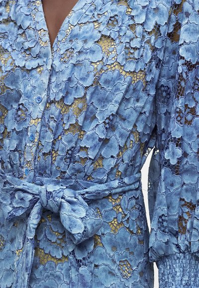 Robe en dentelle florale bleue avec un col en V, des boutons, des manches longues bouffantes et une ceinture nouée à la taille sur une doublure beige.