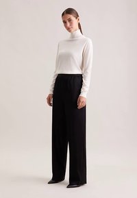 Lichtbeige coltrui van zachte stof gecombineerd met zwarte, wijde broek met hoge taille. Beide kledingstukken hebben een gladde textuur.