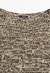 Primo piano di un'etichetta Massimo Dutti su un maglione marrone e beige a maglia larga con motivo testurizzato e intrecciato e scollatura arrotondata.