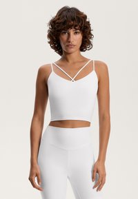 White crop top with thin crossed straps and a fitted design. Smooth texture, minimalist style, pair with high-waisted bottoms.