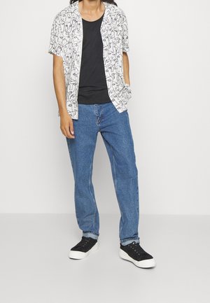 Short-sleeve white shirt with black abstract line pattern, paired with blue jeans and black sneakers with white soles.