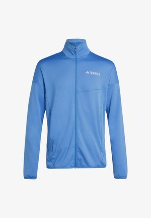 Lichtblauwe jas met volledige ritssluiting, hoge kraag en wit "TERREX"-logo op de linkerborst, lange mouwen en zijzakken.