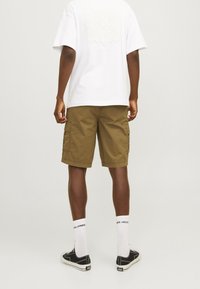 T-shirt blanc avec un motif floral texturé dans le dos, associé à un short cargo kaki avec poches latérales et coupe décontractée. Baskets noires.