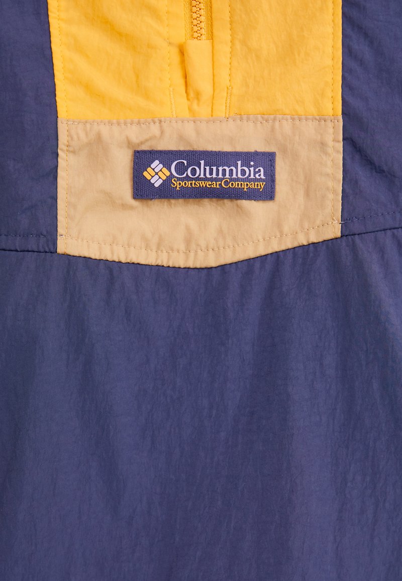 Sudadera de Columbia Sportswear Company con media cremallera, con un cuerpo azul marino, panel amarillo y detalles en color beige; logotipo bordado en la tela.