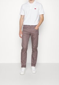 Camisa polo blanca con logo rojo, combinada con pantalones ajustados de color púrpura claro y zapatillas blancas. Tejido suave con diseño clásico de cuello.
