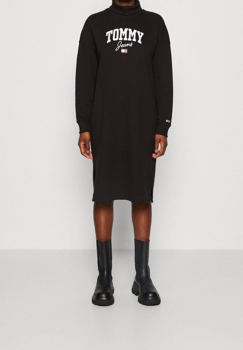 Robe midi noire à manches longues avec col roulé, texte et logo « Tommy Jeans », portée avec des bottines noires épaisses.