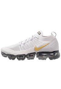 Witte Nike Air Max sneakers met een gebreid bovenwerk en gouden swoosh, met een zwarte podzool voor demping en textuurdetails.