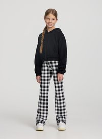 Felpa nera corta con zip, abbinata a pantaloni a vita alta a quadretti bianchi e neri. Scarpe da ginnastica bianche completano il look.