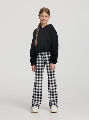 Czarna krótka bluza z kapturem na zamek, zestawiona z wysokim stanem, czarno-białymi spodniami w kratkę. Stylizację dopełniają białe trampki.