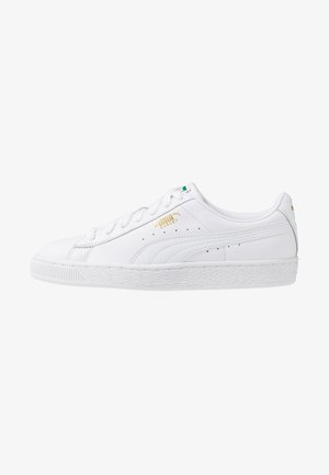 White leather sneakers with a textured white rubber sole, featuring gold branding, a green accent on the tongue, and perforated detailing.