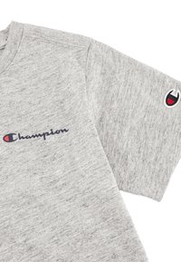 Szara krótki rękaw T-shirt uszyta z miękkiego materiału, z granatowym logo "Champion" z przodu oraz małym, wielokolorowym logo na rękawie.