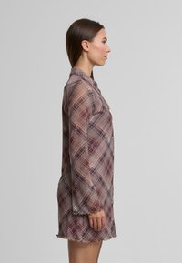 Rochie plisată din material transparent în nuanțe de mov și burgund. Are un închidere cu nasturi, guler, mâneci lungi și un fald ondulat.