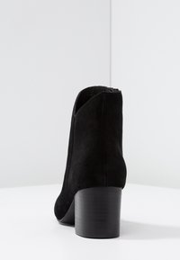 Stivaletto caviglia in suede nero con punta tonda e tacco nero spesso. Texture liscia con un design leggermente incurvato al colletto.