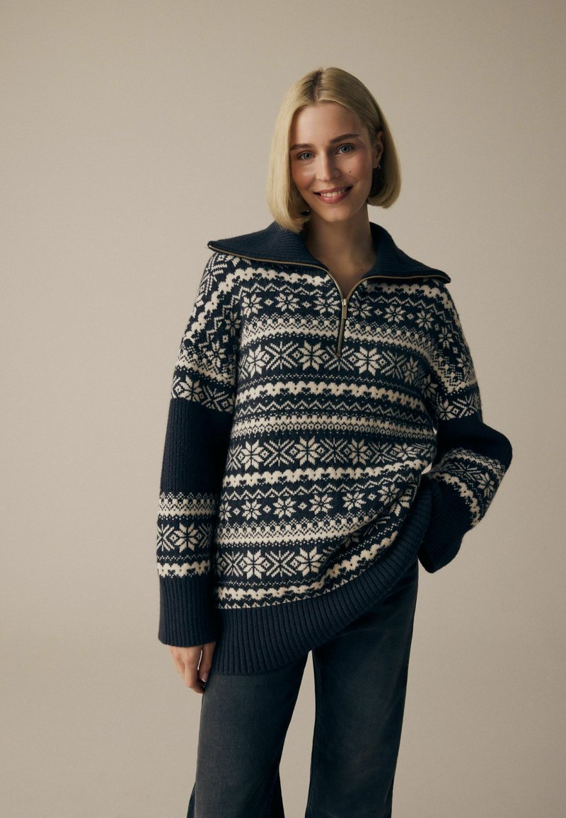Geweven pullover trui in marineblauw met een wit geometrisch Fair Isle-patroon, voorzien van een ritskraag en geribbelde zoom en manchetten, textuurstof.