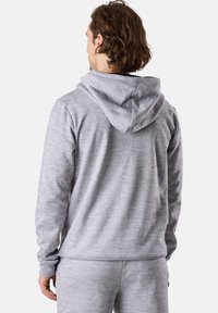 Felpa grigia con cappuccio, caratterizzata da un tessuto testurizzato, polsini a costine e un design semplice, vista da dietro. Abbinata a pantaloni coordinati.