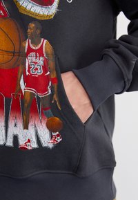 Felpa nera con stampa grafica colorata di un giocatore di basket in uniforme rossa, dotata di tasca frontale e polsini a costine.
