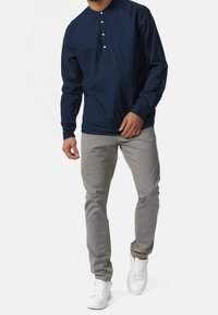 Granatowa koszula henley z długim rękawem i zapięciem na guziki, zestawiona z jasnoszarymi, slim-fit spodniami oraz białymi sneakersami. Gładki materiał i nowoczesny krój.