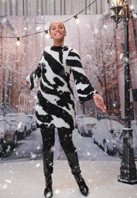 Musta-valkoinen kuviollinen pörröswetterimekko, jossa on leveät hihat, yhdistettynä mustiin polvisukkiin. Taustalla kaupungin katu, jossa sataa lunta.