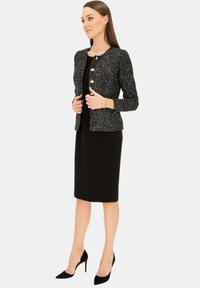 Czarna tweedowa marynarka z wielokolorowymi nitkami, okrągły dekolt i trzy duże guziki, zestawiona z czarną sukienką ołówkową i czarnymi szpilkami.