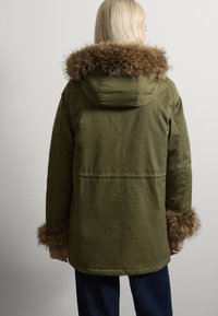 Parka verde oliva con capucha, con un borde de piel sintética en el cuello y los puños; tejido liso, de longitud media y con un corte casual.