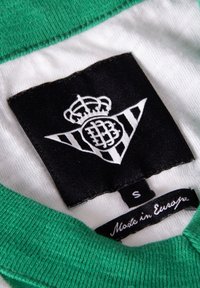 Zwarte tag met een witte logo dat een kroon en strepen bevat, groene kraag, en een label met de tekst "Made in Europe," maat "S."