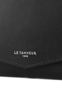 Portafoglio in pelle nera con superficie testurizzata. Presenta il logo in rilievo bianco "LE TANNEUR 1898" e cuciture a contrasto lungo i bordi.