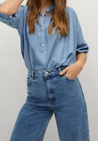Blouse boutonnée bleu clair à coupe décontractée, associée à un jean en denim bleu foncé taille haute avec un design classique à cinq poches.