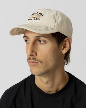 Tan baseball cap with black stitching and embroidered "freedom" text; features a curved brim and adjustable strap at the back.