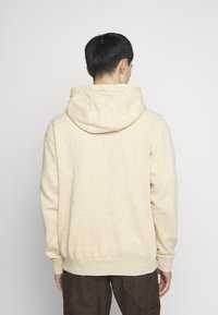 Beige hooded sweatshirt made from textured fabric with visible speckles, featuring a kangaroo pocket and ribbed cuffs and hem.