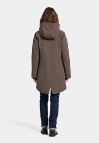 Grijze hooded jacket met een rechte snit, voorzien van een gespleten zoom en gestikte naden, gecombineerd met donkere jeans en zwarte schoenen.