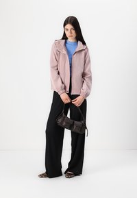 Rosa corduroy-jakke med glidelås foran og hette, paret med en blå ribbestrikket genser, sorte vide bukser og en liten mørk håndveske.
