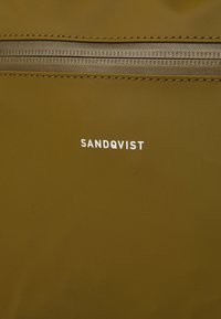 Olajzöld táska, amelynek texturált felszíne van, felül cipzárral záródik, és a "SANDQVIST" fehér logója hangsúlyosan szerepel az elején.
