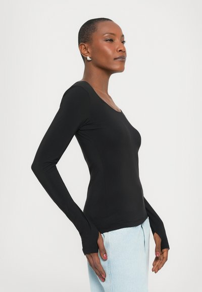 Maglia nera a maniche lunghe con scollo a barca e aperture per il pollice, realizzata in un tessuto liscio, abbinata a jeans a vita alta di colore blu chiaro.