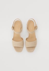 Beige suede slingback sandals with a wide front strap and a rounded toe, featuring an adjustable buckle and a smooth, tan insole.