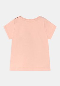 T-shirt de manga curta cor-de-rosa clara em tecido de algodão suave, com decote redondo e três botões decorativos no ombro.