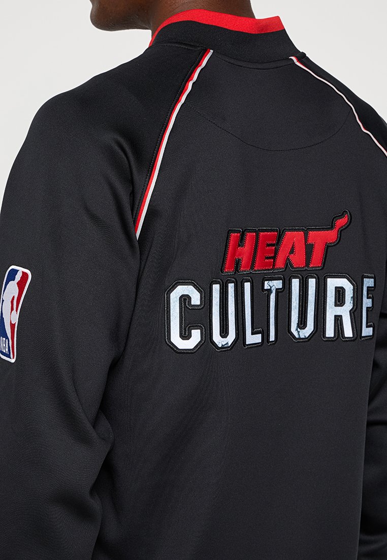 Giacca nera con "HEAT" e "CULTURE" ricamati in rosso e argento. Accentuata da piping bianco lungo le spalle. Logo NBA sulla manica.