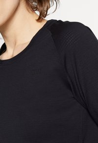 Black athletic shirt featuring a textured fabric, round neckline, and raglan sleeves. Subtle branding on the front left.
