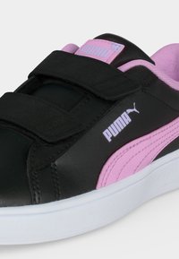 Μαύρο και ροζ αθλητικό παπούτσι Puma με δύο μαύρα λουράκια Velcro και λευκή σόλα, που δείχνει το λογότυπο Puma στο πλάι και στη γλώσσα.