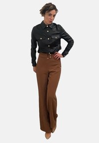 Camicia button-up nera in ecopelle con due tasche sul petto, abbinata a pantaloni larghi a vita alta marroni. Tacchi in tonalità neutra.