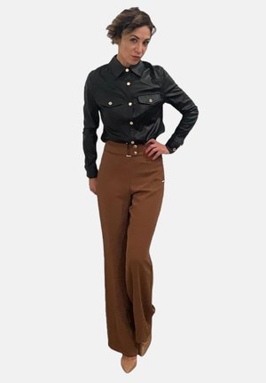 Camicia button-up nera in ecopelle con due tasche sul petto, abbinata a pantaloni larghi a vita alta marroni. Tacchi in tonalità neutra.