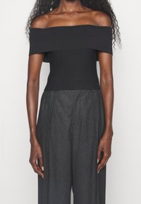 Top nero off-shoulder con texture a costine e design aderente, abbinato a pantaloni grigi a vita alta e dalla vestibilità morbida.