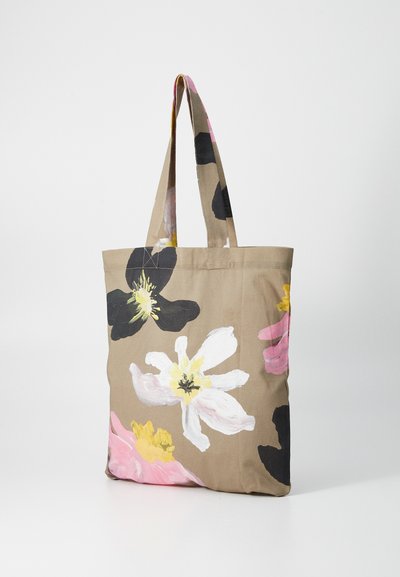 Beige bomullstygspåse med färgglada blommönster som visar vita, rosa och svarta blommor. Två kraftiga axelremmar.