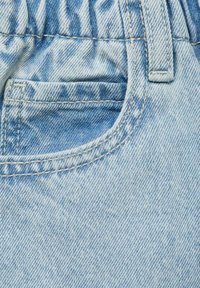 Svetlo modra denimska tkanina z valovito teksturo, ukrivljenim žepom in vidno šivanim robom pasu ter robom žepa.