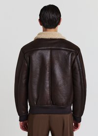 Giacca in finta pelle marrone con colletto in shearling beige, polsini e orlo a coste, texture liscia e silhouette leggermente arrotondata.