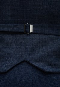 Dunkelblaues Strukturgewebe mit einem subtilen gewebten Muster, versehen mit einem silbernen metallischen Schnallenakzent in der Taille. Scharfe, schräg geschnittene Saumdetails sichtbar.