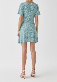Robe courte à manches courtes à motif floral en bleu sarcelle, avec une taille cintrée et une jupe évasée. Elle présente un col rond et une texture légère et lisse.