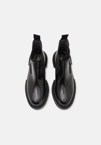Botas de tobillo de cuero negro con paneles laterales elásticos y suelas de goma texturizadas, con punteras redondeadas y tiradores para ponerlas y quitarlas fácilmente.